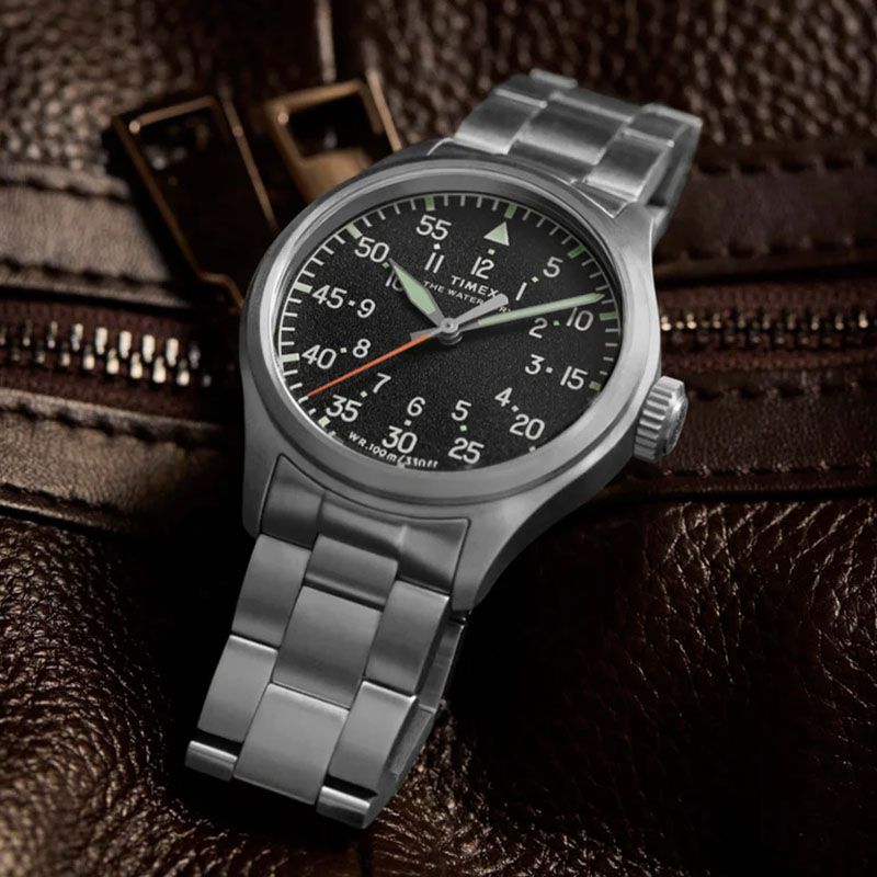 Timex Waterbury Ace TW2Y70300 – zegarek na stalowej bransolecie na tle brązowej skórzanej torby