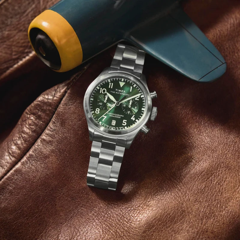 Timex Waterbury Ace Chronograph TW2Y19100 - chronograf na stalowej bransolecie na tle skórzanej kurtki i modelu samolotu